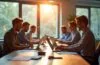 Ein modernes, hell erleuchtetes Büro mit motivierten Mitarbeitenden in entspannter Atmosphäre, die an Laptops und Tablets arbeiten; natürliche Tageslichtstimmung betont einen freundlichen, warmen Workflow zwischen Mensch und innovativer KI-Technologie, die unbemerkt im Hintergrund den digitalen Arbeitsalltag prägt.