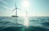 Ein sonnendurchfluteter Morgen am ruhigen Küstenabschnitt mit klar sichtbaren, modernen Offshore-Windrädern vor sanftem Meereshorizont und im Vordergrund technologische, wasserdichte Container, die als Unterwasser-Rechenzentren dienen – ein harmonisches Zusammenspiel von nachhaltiger Energie und Hightech, das in natürlichem Licht Wärme und Fortschritt ausstrahlt.