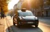 Ein sonnendurchflutetes Straßenszenario in einer lebhaften deutschen Stadt, das einen modernen Tesla in eleganter Fahrt zeigt, während natürliche Lichtreflexe auf dem glänzenden Lack spielen und im Hintergrund freundliche Passanten und urbane Architektur die innovative Zukunft des autonomen Fahrens warm und einladend widerspiegeln.