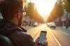 Ein sonnendurchfluteter Straßenabschnitt in moderner Stadtlandschaft, auf dem ein Fahrer entspannt und konzentriert mit Hilfe einer Smartphone-Navigation die Spur wechselt, während sanftes Tageslicht die urbane Dynamik und freundliche Atmosphäre lebendig einfängt.