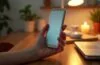 Ein lebendiges, natürlich beleuchtetes Bild eines eleganten, kompakten faltbaren Smartphones in metallischem Design, das behutsam in einer hellen, warmen Hände gehalten wird, umgeben von sanft verschwommenen Alltagsgegenständen auf einem modernen Holztisch, das eine Mischung aus technologischem Fortschritt und menschlicher Nähe ausstrahlt.
