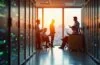 Ein freundliches, hell erleuchtetes Büro mit modernen Server-Racks und mehreren konzentrierten IT-Spezialisten, die in entspannter Atmosphäre gemeinsam komplexe Cybersecurity-Strategien für eine KI-Infrastruktur besprechen, während Sonnenlicht sanft durch große Fenster fällt und Wärme und Hoffnung auf sichere digitale Zukunft verströmt.
