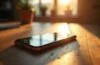 Ein hell erleuchtetes, modernes Smartphone auf einem warmen Holztisch, umgeben von sanftem Tageslicht und sanften Schatten, das in einem offenen, freundlichen Arbeitsumfeld die Verschmelzung von KI-Technologie und Datenschutz symbolisiert.