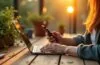 Ein warm ausgeleuchtetes, authentisches Portrait einer jungen Person, die entspannt mit einem minimalistischen Dumbphone in der Hand auf einem sonnendurchfluteten Holztisch sitzt, umgeben von natürlichen Elementen wie Grünpflanzen und einem Kerzenlicht, das eine ruhige digitale Auszeit und bewusste Entschleunigung inmitten des modernen Alltags symbolisiert.
