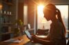 Ein warm beleuchtetes, modernes Büro mit einer jungen Frau, die mit aufmerksamem, leicht nachdenklichem Blick auf ihr Smartphone schaut, während im Hintergrund durch ein großes Fenster sanftes Tageslicht fällt und eine angenehme, vertrauensvolle Atmosphäre digitaler Kommunikation vermittelt.