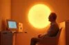In einem hell erleuchteten Healthspan-Studio sitzt eine sympathische Person entspannt unter sanft warmem Infrarotlicht, umgeben von moderner Biofeedback-Technologie und digitalen Messgeräten, die mit natürlicher Tageslichtstimmung ein Gefühl von Hoffnung, Innovation und lebensverlängernder Selbstfürsorge vermitteln.