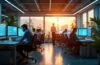 Ein hell erleuchtetes, modernes Büro mit Mitarbeitern in konzentrierter, aber entspannter Atmosphäre, die gemeinsam vor großen Bildschirmen an digitalen Sicherheitsstrategien arbeiten, umgeben von warmem Tageslicht und organischen Pflanzen, das die Bedeutung der NIS2-Cybersicherheitsrichtlinie für Unternehmen lebensnah und zugänglich vermittelt.