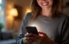 Ein strahlend beleuchtetes Smartphone in der Hand einer Person, die lächelnd mit einer lebhaften Chat-App interagiert, umgeben von warmem Tageslicht und einer modernen, einladenden Wohnumgebung, die die faszinierende Verschmelzung von menschlicher Kommunikation und smarter KI-Technologie eindrucksvoll vermittelt.