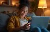 Ein modernes Wohnzimmer mit einer jungen, nachdenklich lächelnden Person, die ein Smartphone und Laptop benutzt, umgeben von warmem Tageslicht und dezenten technischen Gadgets, die den Alltag und die steigenden Technologiekosten 2026 spiegeln.