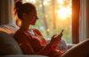 Ein hell erleuchtetes, warmes Wohnzimmer mit einer entspannt wirkenden Person, die sorgsam ihr Smartphone prüft, während natürliches Tageslicht sanft durch ein Fenster fällt und eine Atmosphäre von Vertrauen und Aufmerksamkeit schafft.
